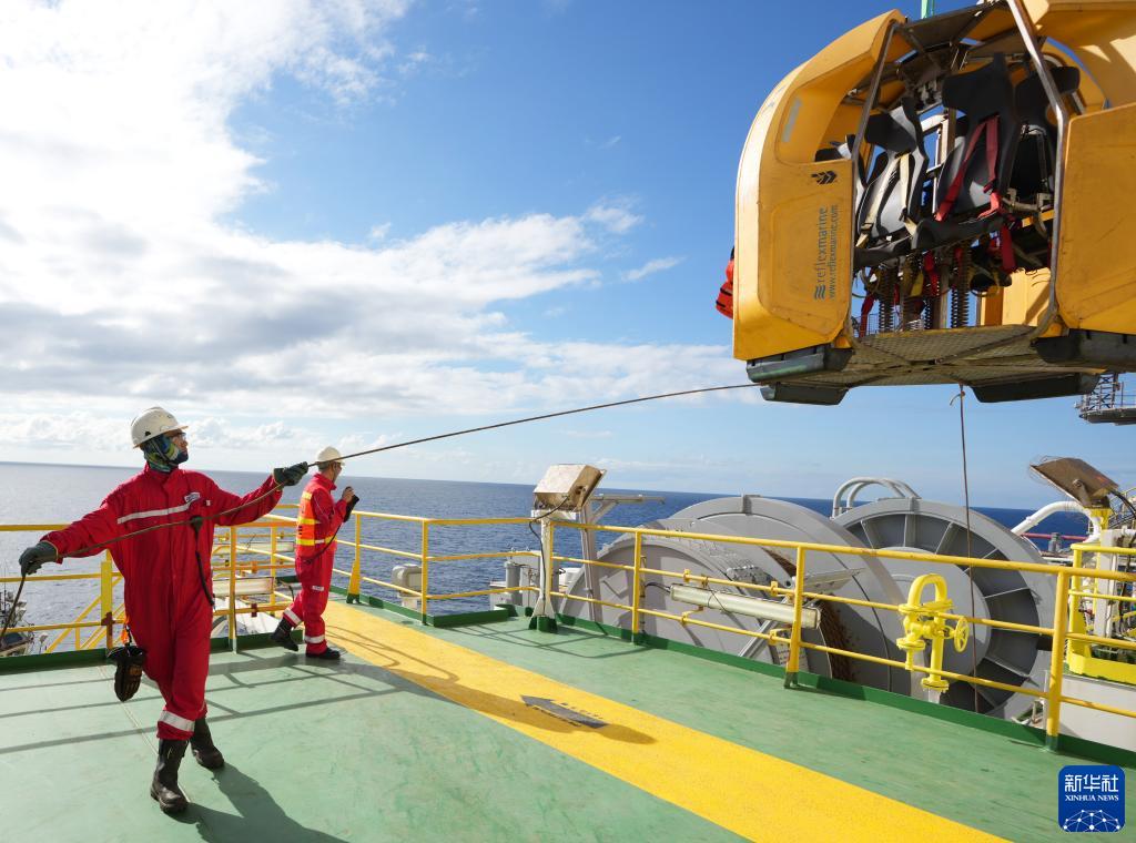 工人在"海洋石油982"半潜式钻井平台上拉住吊笼,准备运送工友去作业